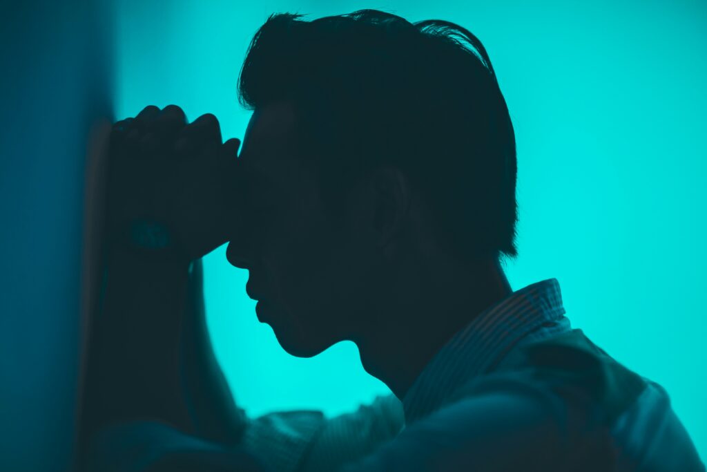 Silhouette of a man holding his head in distress against a blue background, representing emotional pain related to chronic headaches and anxiety.