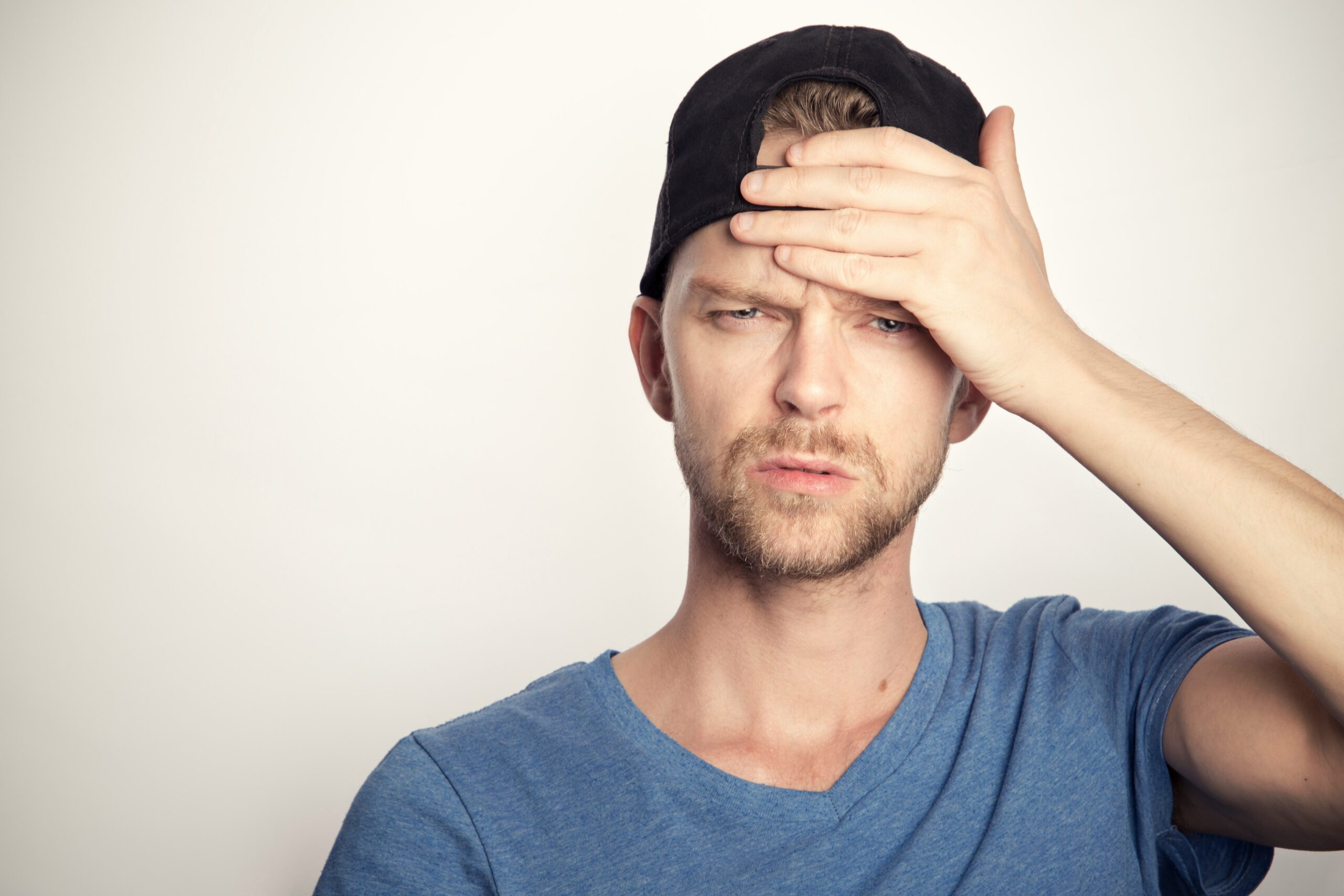 Man in a blue shirt and cap holding his forehead, expressing discomfort, symbolizing headache pain relevant to headache treatment information in Parma, Ohio.