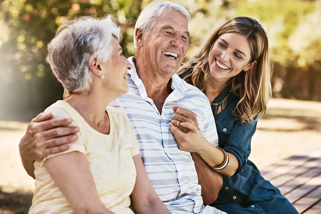Elderly couple smiling with adult daughter in a park, reflecting joy and family support in managing chronic pain and enhancing quality of life.