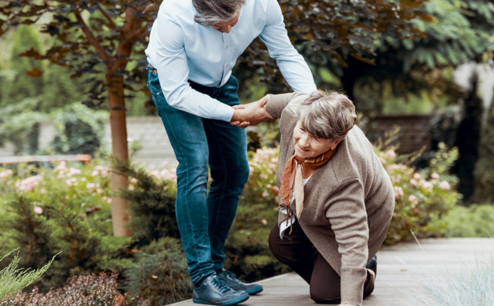 Man assisting older woman who has fallen, highlighting balance issues related to neuropathy in outdoor setting.